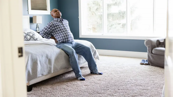 image of man sitting on bed holding his hands on his lower back
